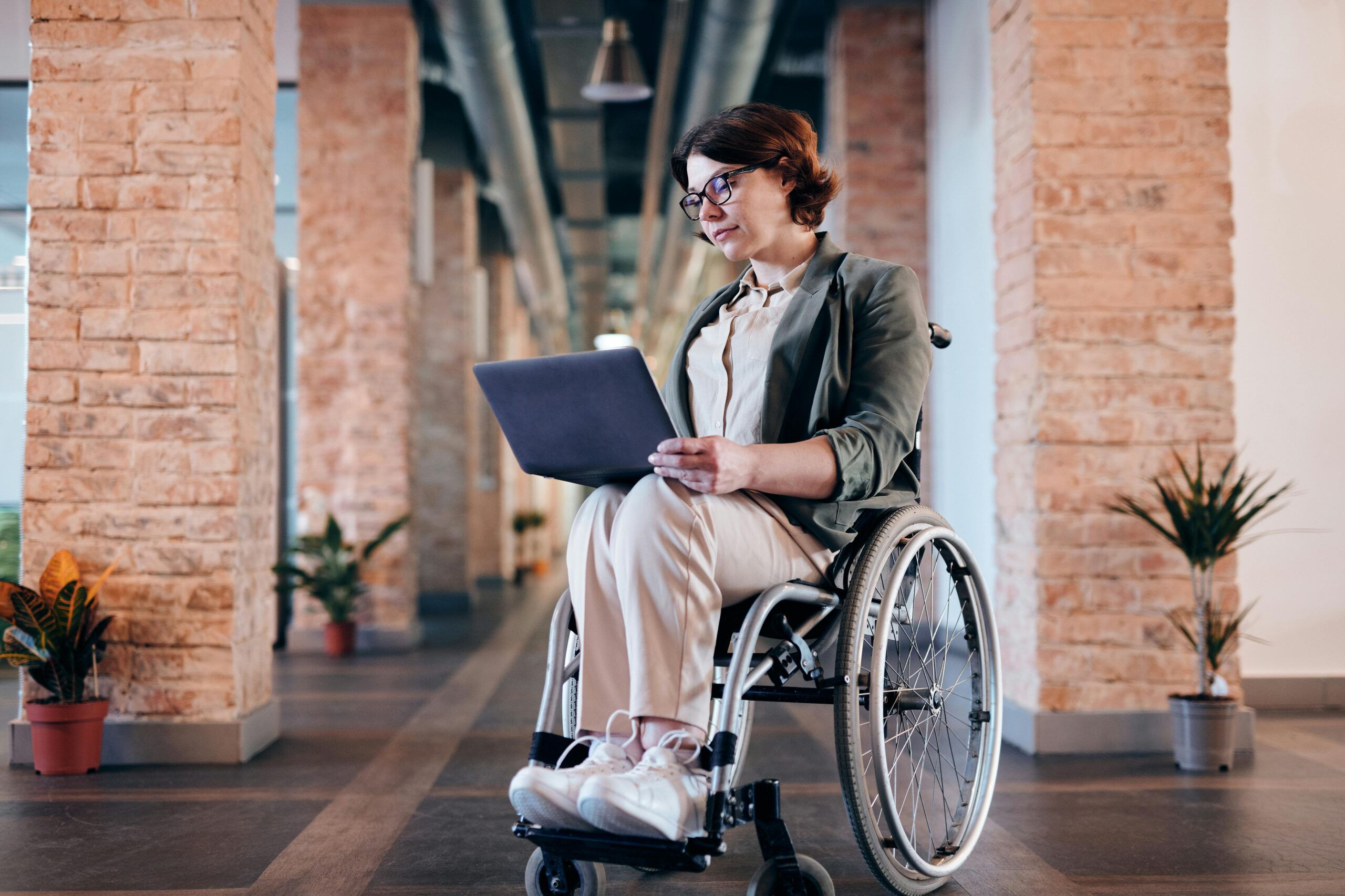Businesswoman in wheelchair using laptop indoors, showcasing modern remote work setup.